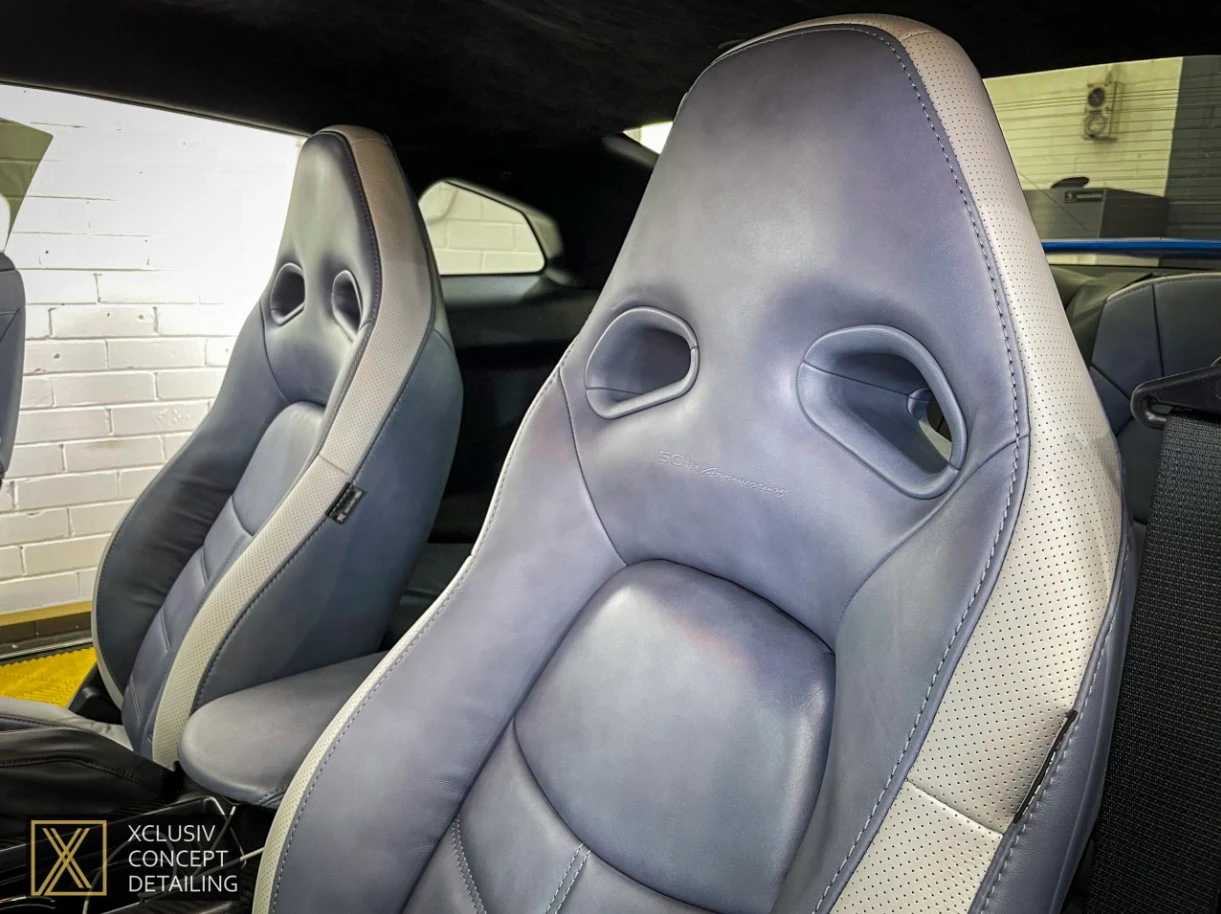 Close-up of two modern car seats with light gray and white leather upholstery, featuring sporty design and ventilation holes. The seats appear clean and well-maintained inside a vehicle.