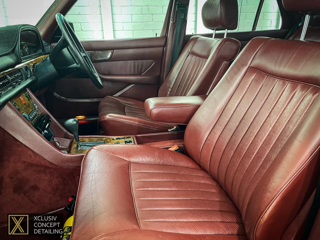 The image shows the clean, detailed interior of a car featuring two front seats with grey, diamond-patterned upholstery. The car door is open, and a logo for Xclusiv Concept Detailing is visible in the bottom left corner.